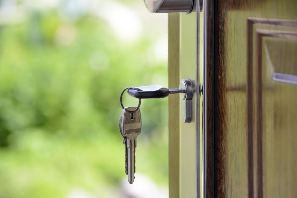 Keys on a ring in the lock of an open wooden door, with a garden blurred behind