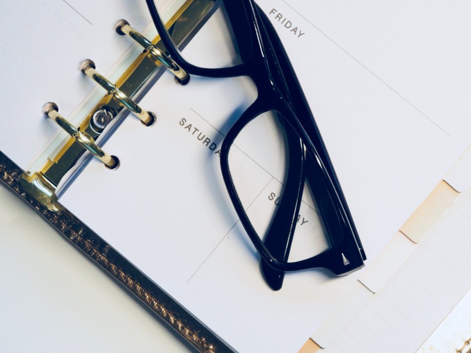 Weekly planner open at Friday, Saturday and Sunday with a pair of glasses resting on it