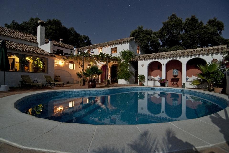 White villa with terracotta roofs and a swimming pool, lit up in the evening